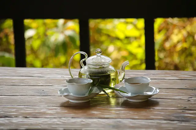 Bamboo Tea in a glass tea pot with two cups on saucers on a wooden table