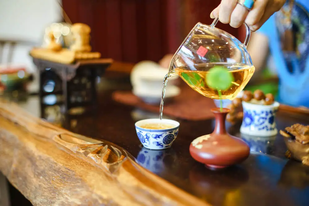 A hand pouring Lapsang Souchong Tea into a cup from a glass teapot.